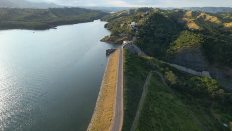 Vuelo-De-Drones-Sobre-Presa-Con-Camino-De-Lago-En-Santiago-De-Los-Caballeros-Al-Atardecer