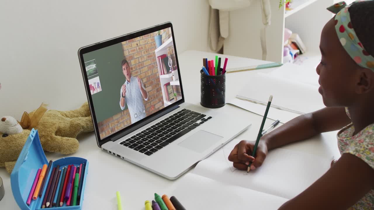 African american girl doing homework while having a video call with male teacher on laptop at home
