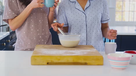 Gleichgeschlechtliches-Weibliches-Paar-Im-Pyjama,-Das-Morgens-Pfannkuchen-Zubereitet-Und-Zu-Hause-In-Der-Küche-Kaffee-Trinkt