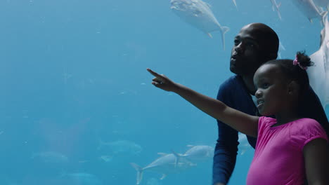 father with little girl at aquarium looking at fish tank teaching curious child about sea life dad showing daughter marine animals in oceanarium