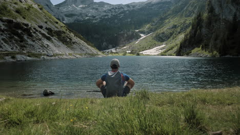 Camera-tracking-forward-towards-the-lake-where-a-hiker-is-sitting-and-looking-at-the-valley