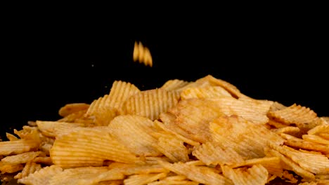 Ridged potato chips fall onto a pile in slow motion, captured in close-up with dramatic studio lighting and a seamless black background for high contrast