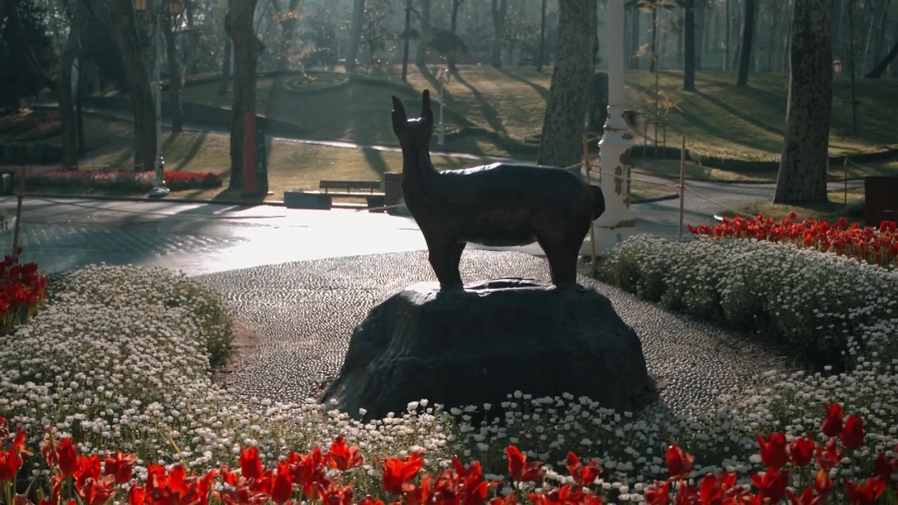 Scultura di cervo su base di pietra circondata da fiori rossi e bianchi in una mattina di sole a Istanbul, Turchia. Primo piano, inquadratura ampia.