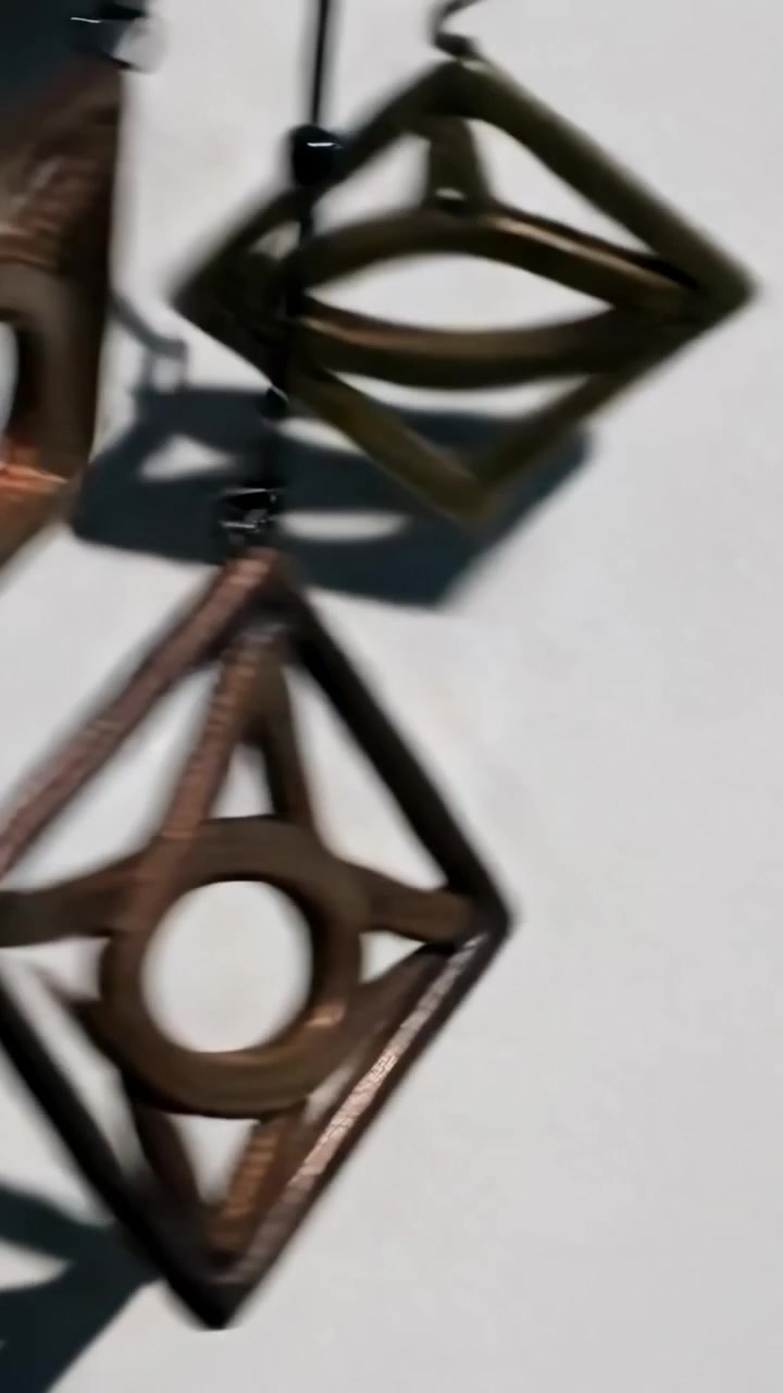 Video verticale: Pendenti metallici in movimento mentre l'ombra si sposta, proiettando forme su una parete bianca, spazio per il testo.