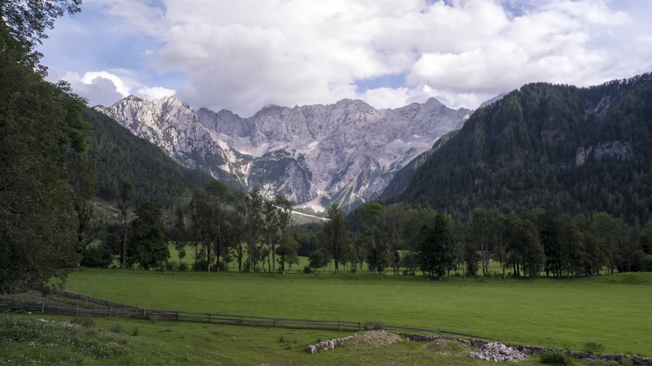 Catena montuosa delle Alpi di Kamnik e della Savinja vista da Zgornje Jezersko in Slovenia, timelapse di nuvole sopra montagne e prati con alberi in primo piano