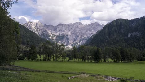 Mountan-range-of-Kamnik-Savinja-Alps-seen-from-Zgornje-Jezersko-in-Slovenia,-Timelapse-of-clouds-above-mountains-and-meadows-with-trees-in-front