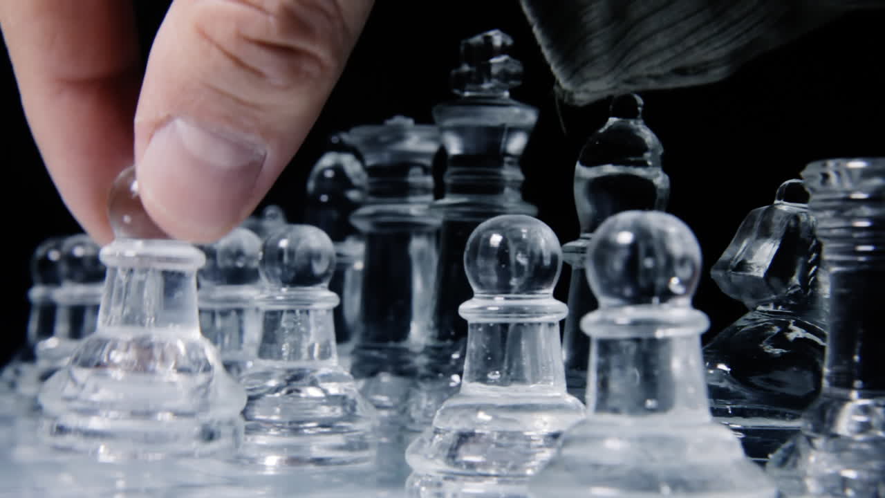 게임의 첫 번째 움직임을 하기 위해 체스판에서 유리 보병을 조심스럽게 뽑는 플레이어의 손