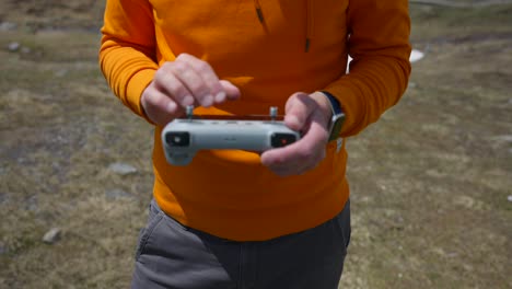 Close-up-shot-of-unrecognizable-man-with-orange-colored-jumper-piloting-drone-using-remote-controller-by-touching-screen-with-fingers