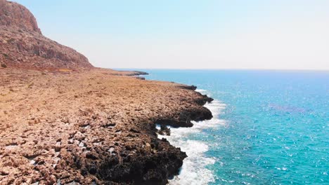 Drone-shot-flying-over-sea-waves-crashing-against-the-rocky-shore-at-Cavo-Greko,-Cyprus