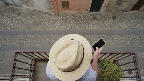 woman using smartphone drinking coffee enjoying summer vacation browsing online messages relaxing on balcony texting wearing hat top view