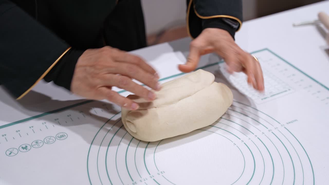 Primo piano di mani che impastano l'impasto del pane su un tappetino da pasticceria al chiuso, mostrando la preparazione casalinga del pane, la consistenza morbida dell'impasto e la preparazione manuale del cibo su una superficie di lavoro della cucina.