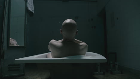 pale bald skinny man takes a bath in the creepy old bathroom at night