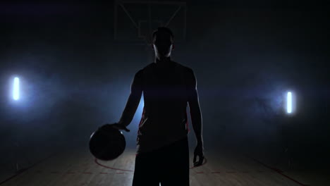Männlicher-Basketballspieler,-Der-Sich-Im-Rauch-Vor-Der-Kamera-Bewegt-Und-Den-Ball-In-Zeitlupe-Mit-Steadicam-Aufnahme-über-Den-Parkettboden-Wirft