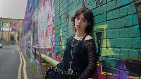 retrato de moda al aire libre de una mujer joven de estilo alternativo apoyándose en una pared cubierta de graffiti en la calle de la ciudad de londres, reino unido, en tiempo real.