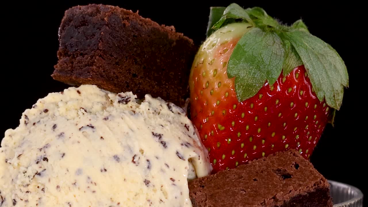 Una mano posiziona attentamente una fragola intera su gelato alla vaniglia con pezzi di brownie