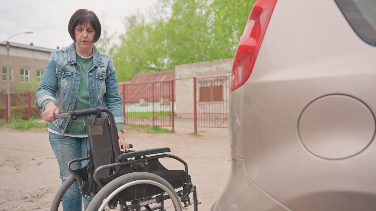 Woman Preparing Wheelchair Beside Car Trunk, Folded Black Seat Near Bumper, Focused Caregiver Adjusting Frame For Transfer, Quiet Parking Lot Ambiance, Mobility Independence Moment
