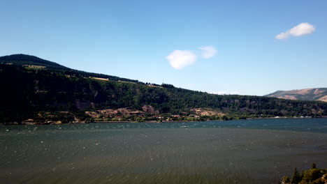 Luz-Del-Sol-En-Las-Tranquilas-Aguas-Del-Lago-Con-Bosque-Verde-Y-Montaña-En-El-Fondo