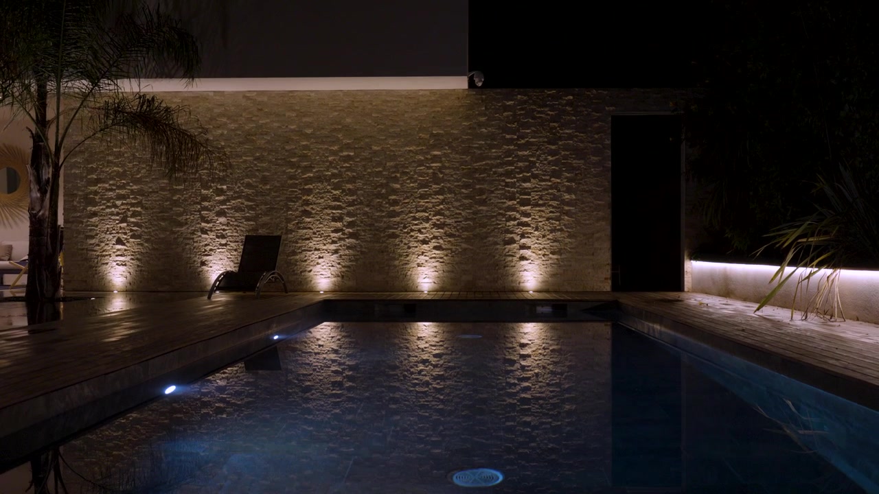 Slow rising shot at night of a lit up garden and pool at a French villa