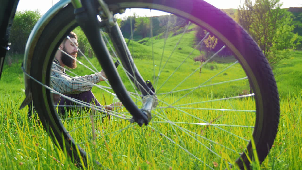 한 젊은 힙스터 남자가 자전거 근처의 초원에서 쉬고 있다