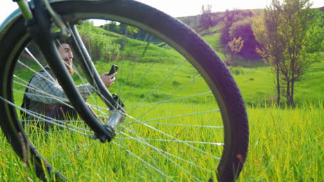 a young hipster man rests in a meadow near a bicycle