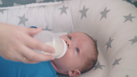 mommy gives bottle with milk to crying baby in soft cocoon