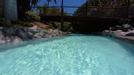 Lazy-River-Ride-In-A-Water-Park-With-Crystal-Clear-Blue-Water-And-Lush-Vegetation-On-The-Side