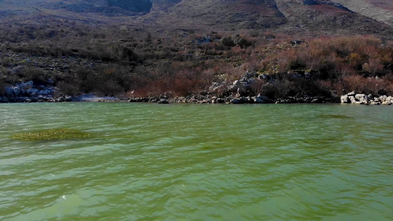 Bird watching tower on rocky shore full of dry bushes and big cliffs with lake view seen from vibrant emerald water of Lake Scadar