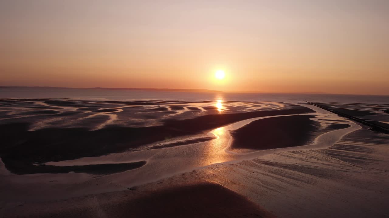 Suggestivo tramonto rosa che si riflette su piccoli corsi d'acqua sulla spiaggia.