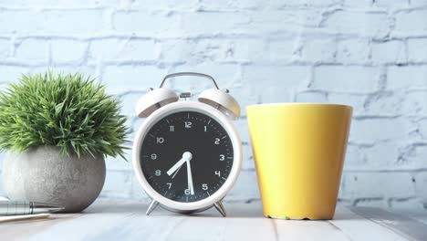 alarm clock, coffee cup, and plant on a desk