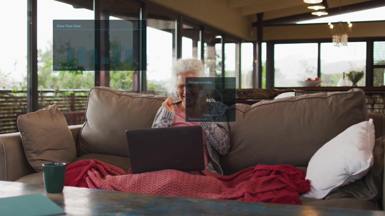 Senior woman sitting sofa with phone watching laptop, call causing HUDs rising for data monitoring
