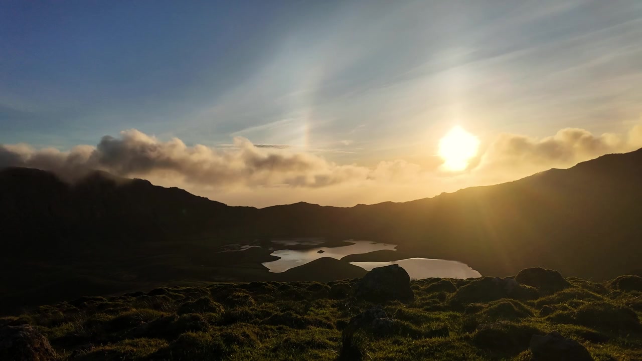Nuvens ao pôr do sol flutuam sobre um lago de caldeira vulcânica e colinas acidentadas na paisagem remota dos Açores