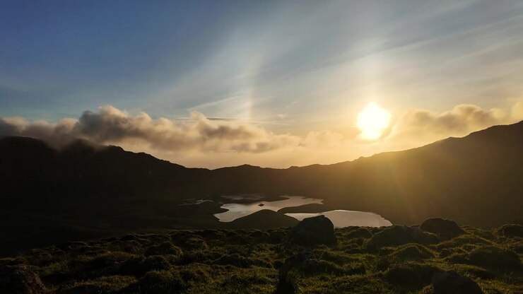 Nubes al atardecer flotan sobre un lago de caldera volcánica y colinas escarpadas en un paisaje remoto de las Azores.