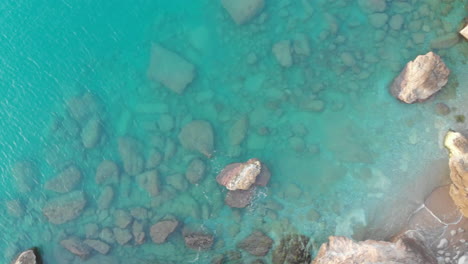 Die-Drohne-Aus-Der-Vogelperspektive-Erfasst-Den-Rand-Einer-Klippe-über-Einer-Zerklüfteten-Landschaft-Aus-Blauem-Wasser-Und-Einer-Weißen-Steinmauer