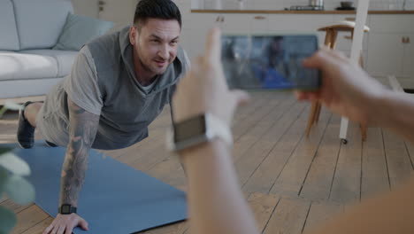 man doing push-ups at home, being filmed by a woman.