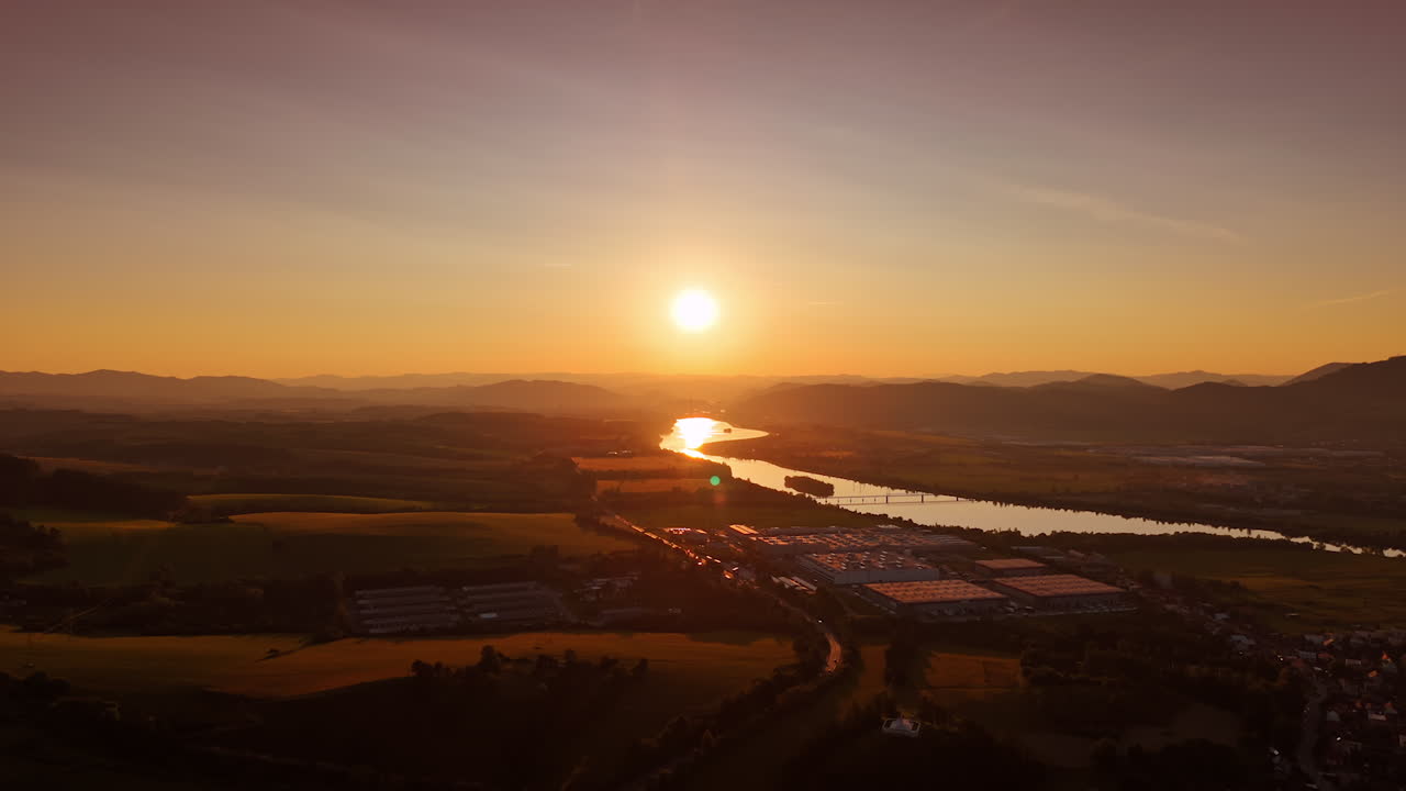 Beautiful sunset over the river valley. Golden sunlight reflects on the river as the sun sets behind distant mountains, illuminating the landscape