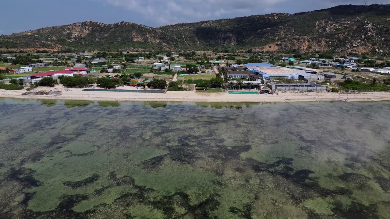 drone flies forward facing down then with an upward pan, revealing the beach and ahead, distant mountains, and a clear horizon in Vietnam
