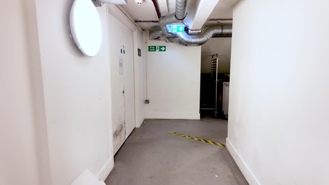 Empty office basement corridor with ventilation pipes and emergency exit signs