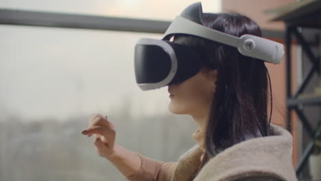 Woman-in-a-helmet-of-virtual-reality-against-the-background-of-a-huge-window-in-the-office-at-the-workplace.-Architect-working-in-a-virtual-reality-helmet.