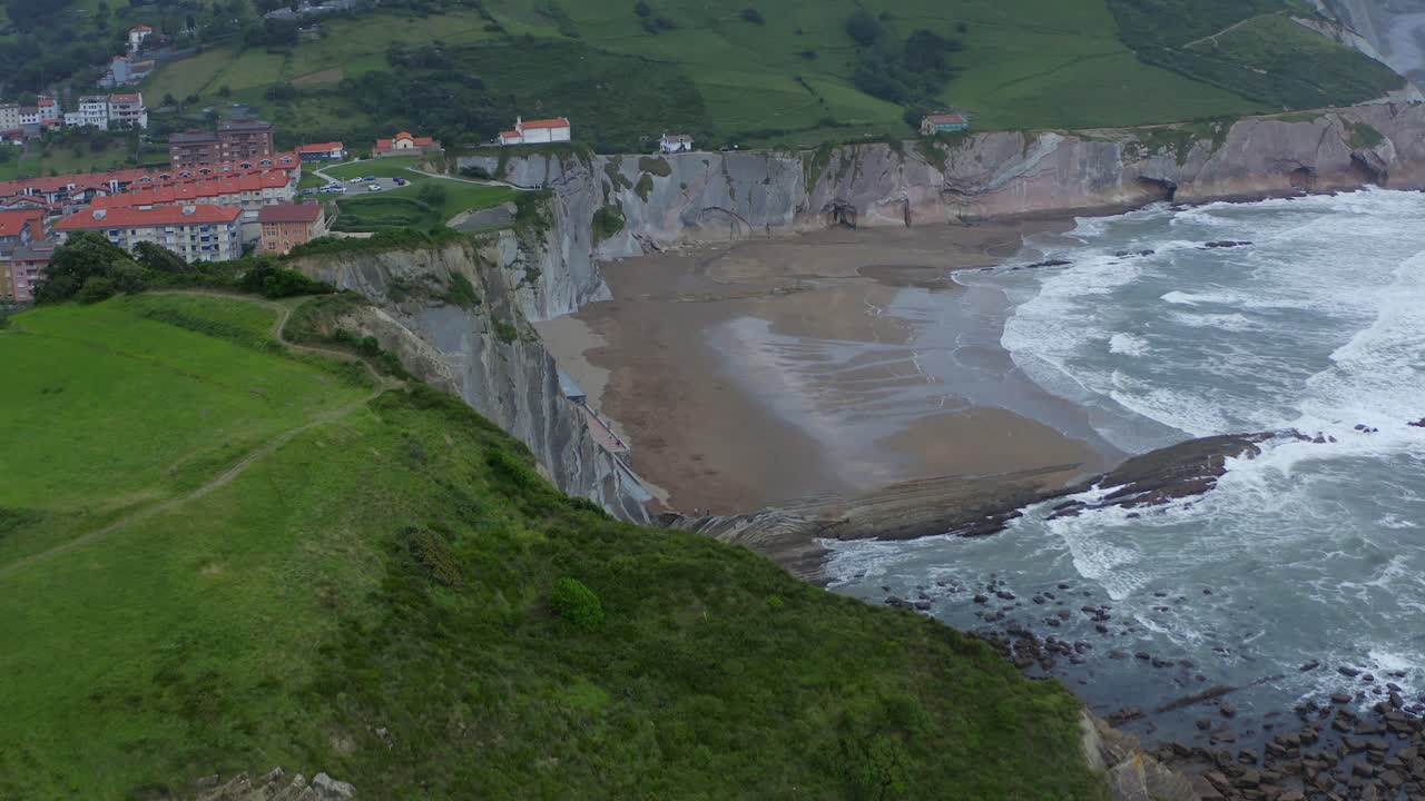 Panoramic drone dolly above green cliffside reveals itzurun beach, cloudy day