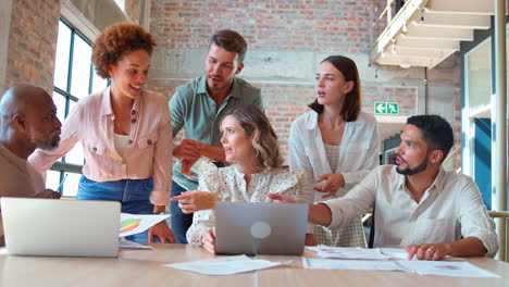 multi-cultural business team meeting around laptop discussing documents in busy office