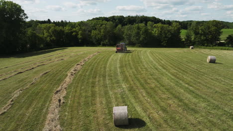 El-Heno-De-Paja-Rueda-Sobre-Los-Campos-Con-Un-Tractor-Empacador-En-Funcionamiento-En-El-Fondo