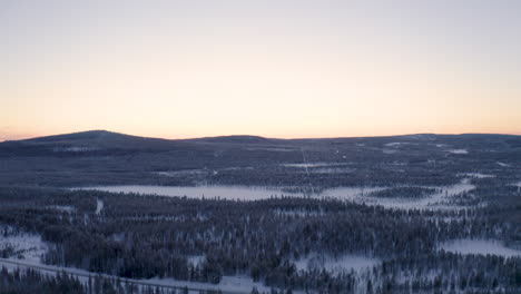 Aerial-view-looking-down-over-Scandinavian-woodland-landscape-tilt-up-reveal-snow-covered-mountain-range-wilderness