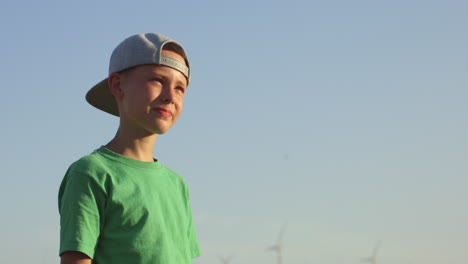 Boy in green t-shirt and cap looking at wind turbines