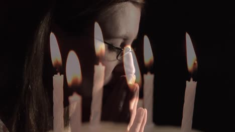 composite video of burning candles against close up of a caucasian woman praying