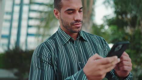 Young-man-texting-on-smartphone-sitting-in-bench-outdoors.