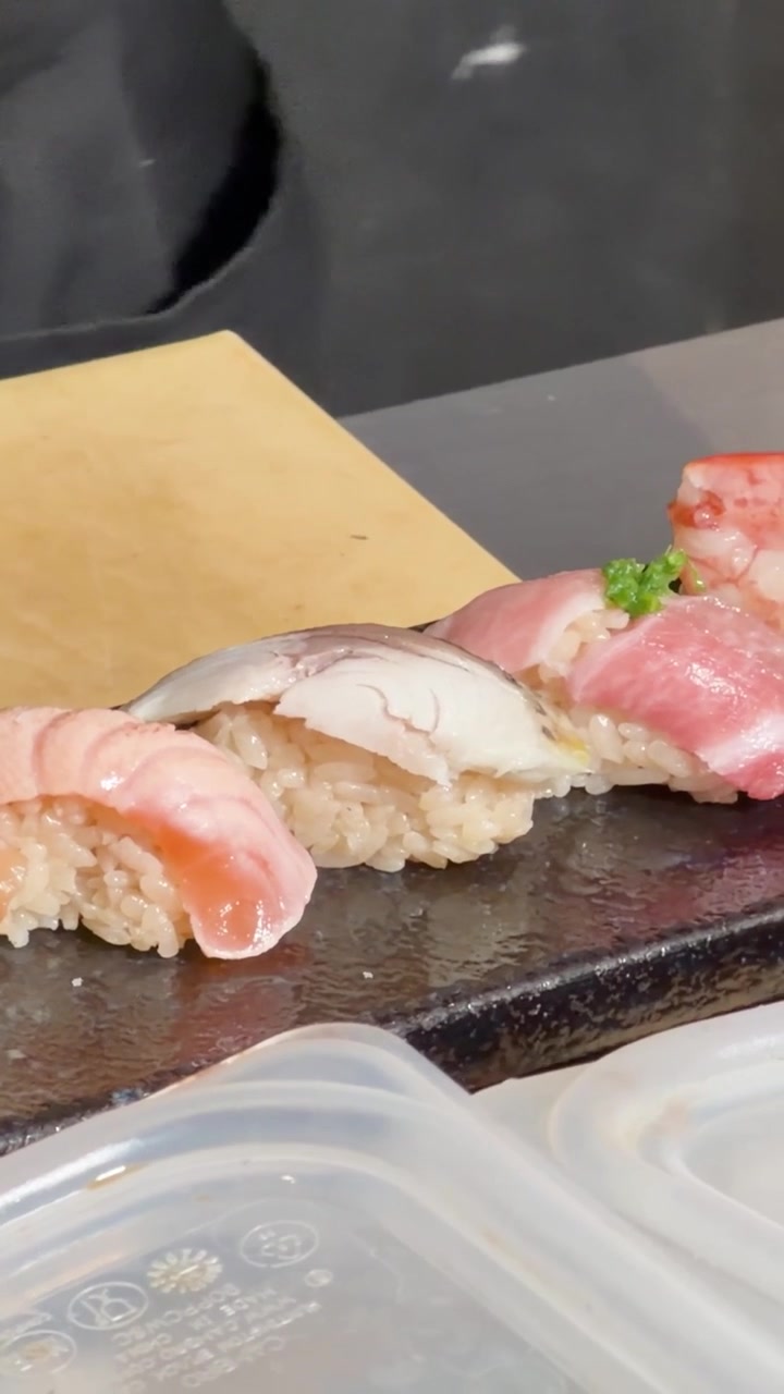 Nahaufnahme der Hände eines Kochs, der sorgfältig frisches Lachs- und Meeresfrüchte-Nigiri auf einer Platte anrichtet