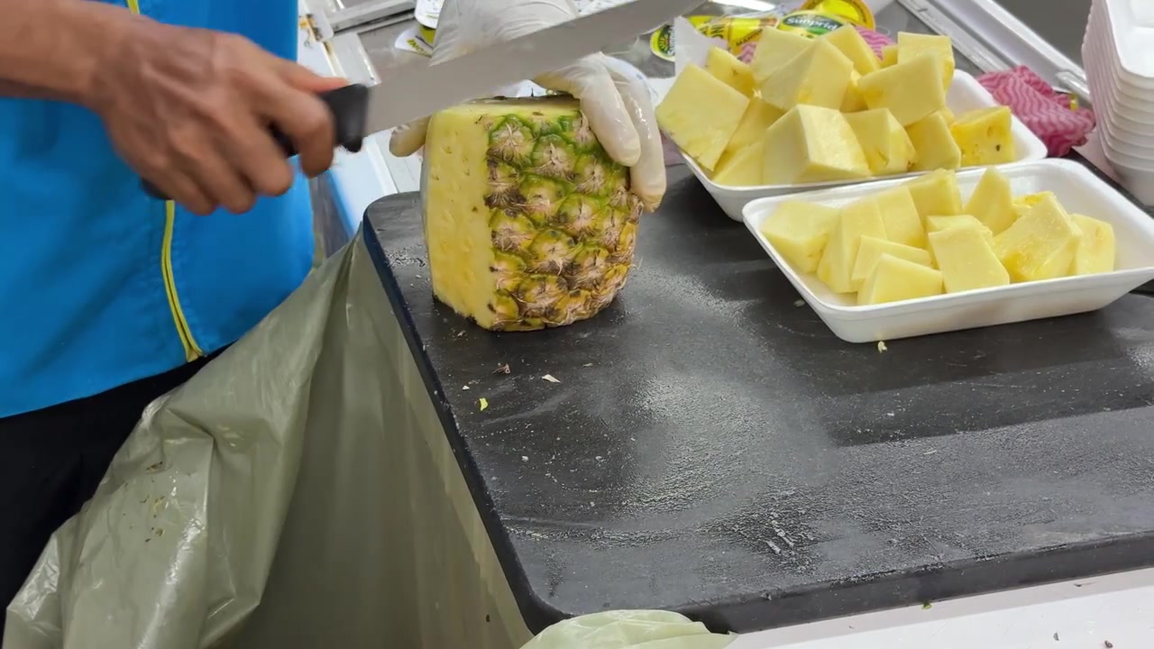 Worker Peeling and Cutting Fresh Pineapple in a Commercial Kitchen