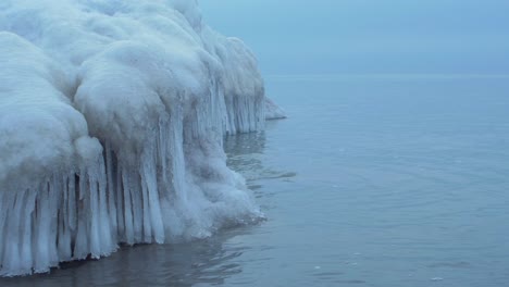 small waves breaking against the ruins of karosta northern forts fortification on the shore of baltic sea on a cloudy winter day, covered with ice, snow and icicles, medium closeup shot