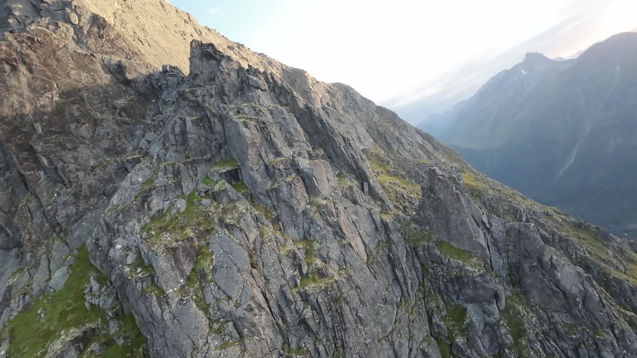 el dron fpv asciende a una cresta de la montaña al atardecer, pintando el cielo con tonos cálidos, capturando un viaje cinematográfico al crepúsculo sobre los picos