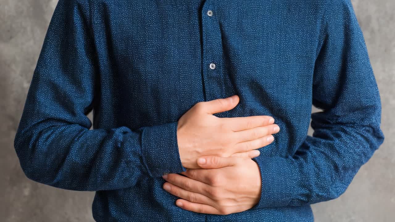 A Man in a Blue Shirt Reflects Discomfort, Holding His Stomach, Suggesting Possible Indigestion or Gastric Distress, Portraying a Sense of Unease in a Neutral Setting